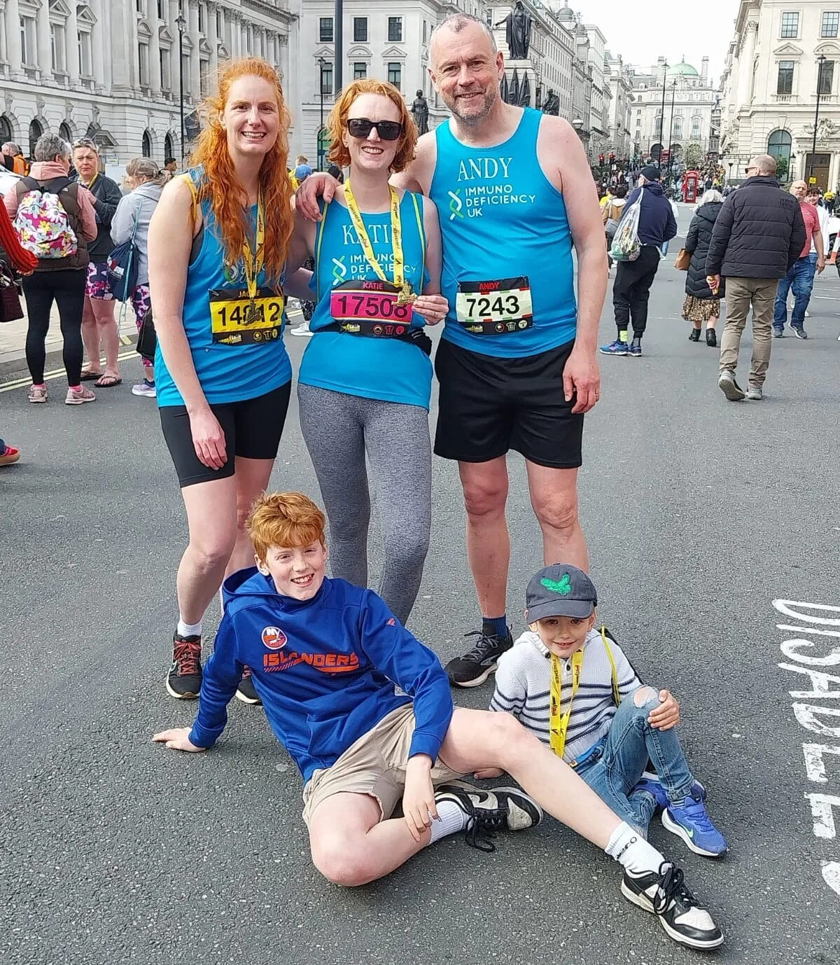 2ad6c0ff-9906-4486-b901-9a25391179d3 Three adults in running kit standing with two children laying on the ground